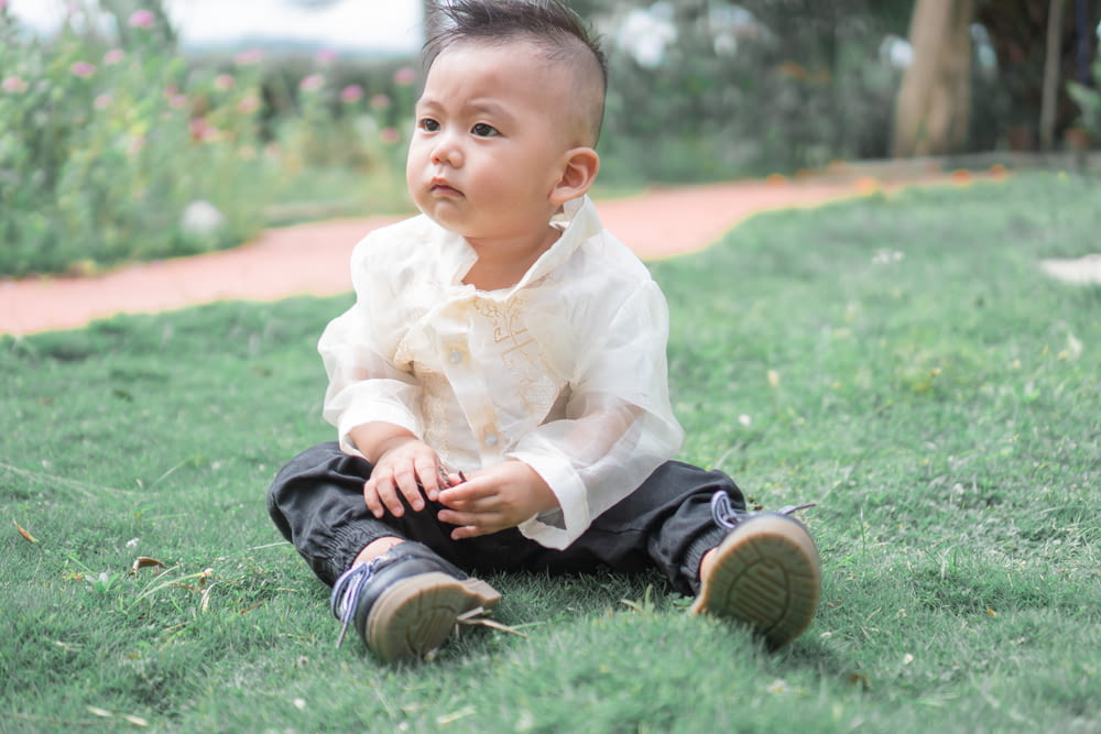 baby in white dress shirt and black pants sitting on green grass during daytime