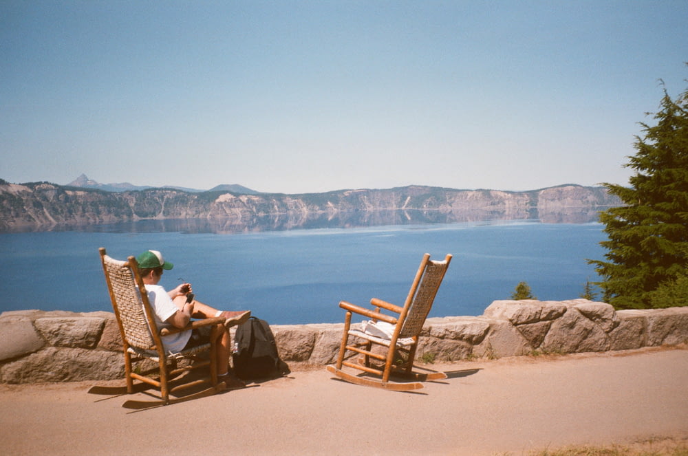 2 person sitting on brown wooden rocking chairs on brown sand near body of water during