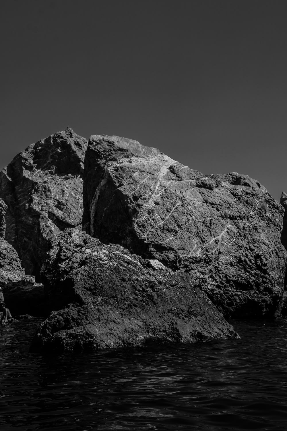 grayscale photo of rocky mountain near body of water