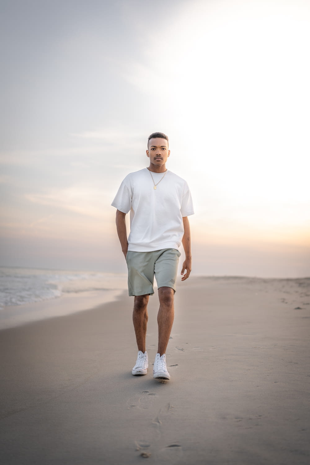 man in white crew neck t-shirt and green shorts standing on beach during daytime