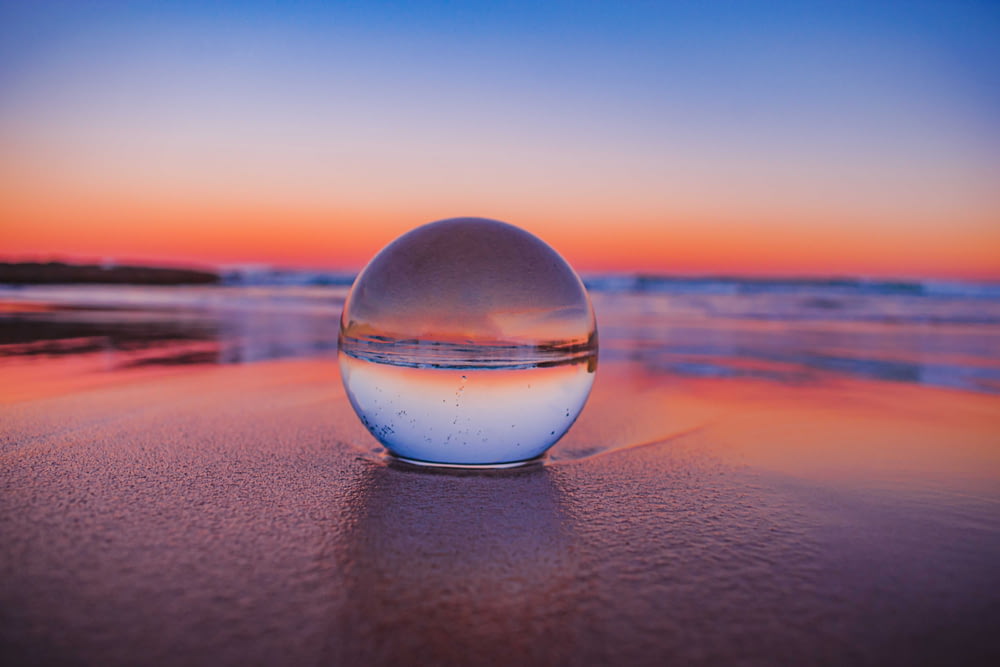 Bola de vidrio transparente sobre arena gris durante la puesta del sol