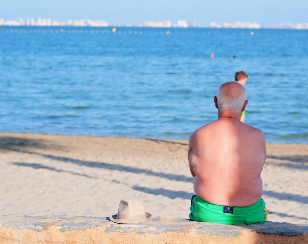man in green shorts sitting on beach during daytime