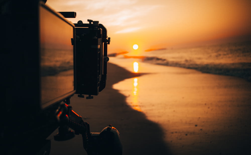 black camera on tripod by the beach during sunset
