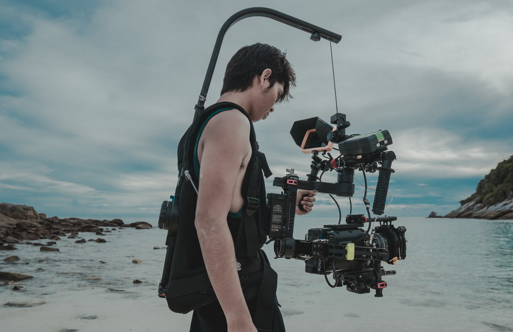 man in black tank top and black shorts holding black dslr camera standing on beach during