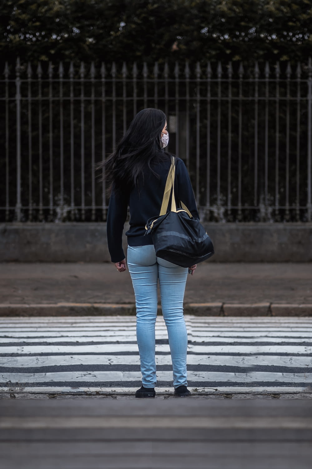 검은 가죽 재킷과 파란색 데님 청바지를 입은 여자가 낮 동안 보행자 차선을 걷고 있다