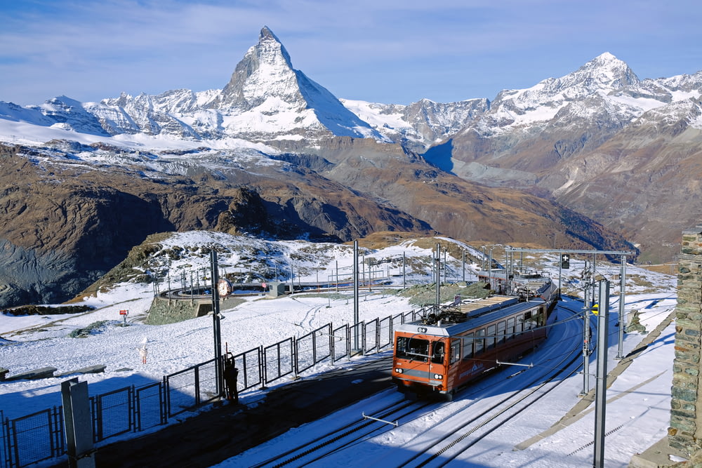 Tren rojo y negro en el riel cerca de la montaña cubierta de nieve durante el día