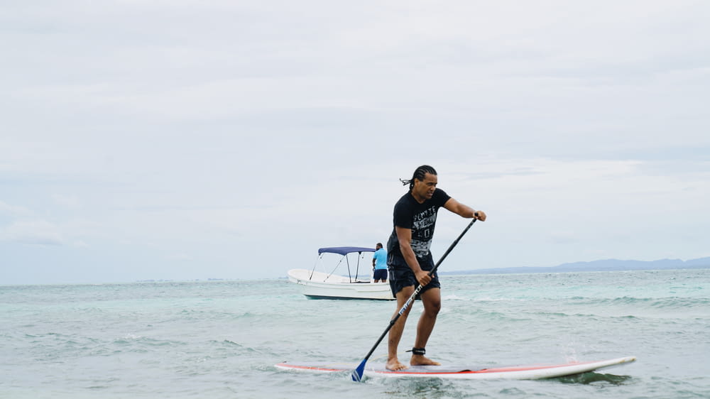 man in blue and black jacket and black pants riding white and red surfboard during daytime