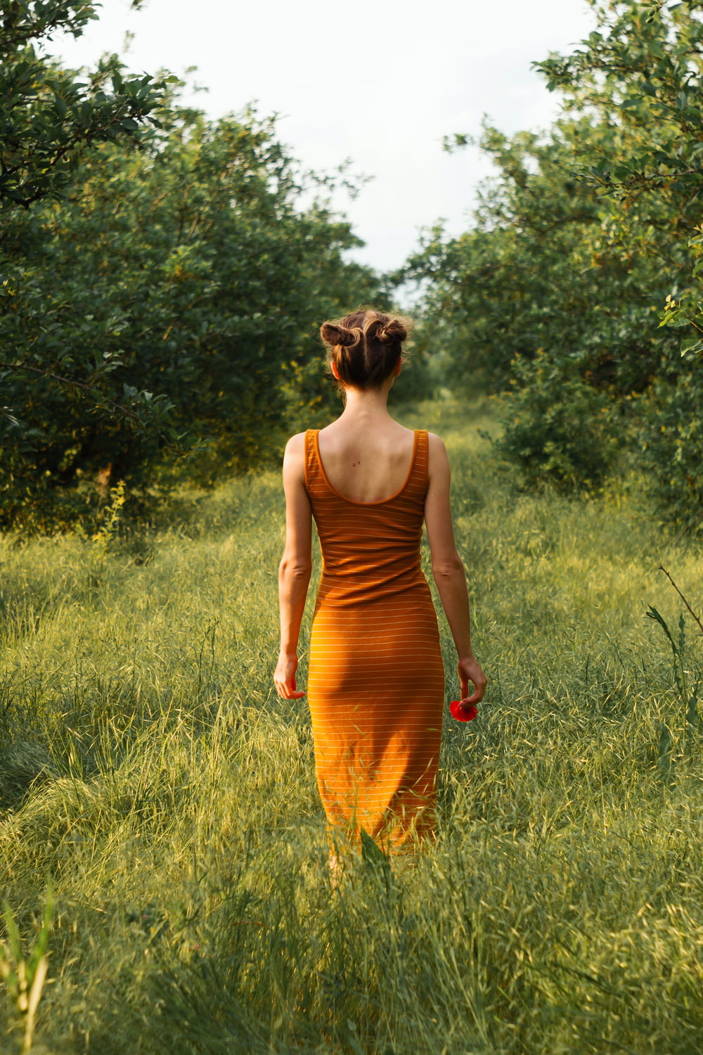 Mujer en vestido naranja sin mangas de pie en el campo de hierba verde durante el día