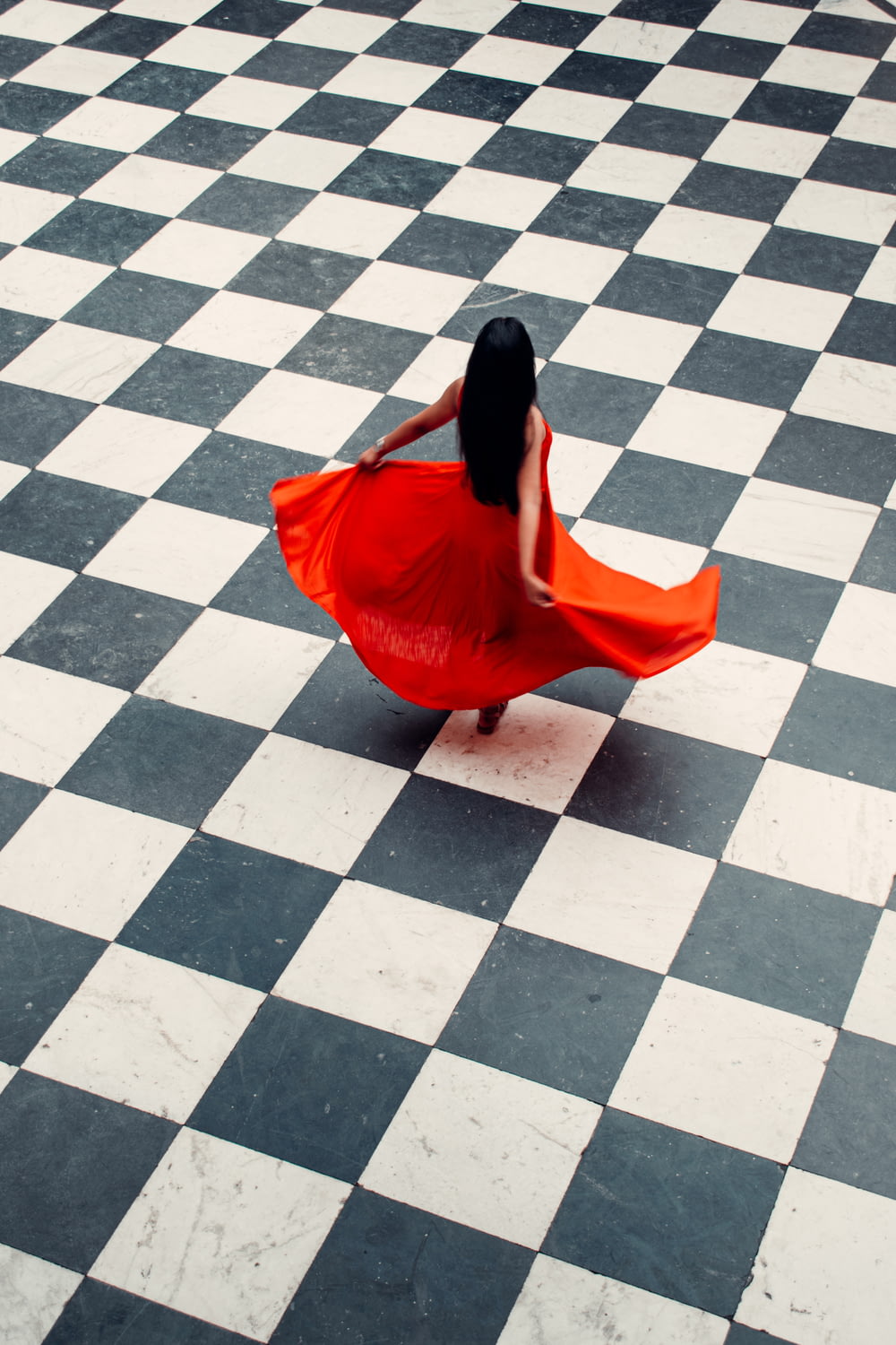 Donna in vestito rosso che cammina sulle piastrelle grigie e bianche del pavimento