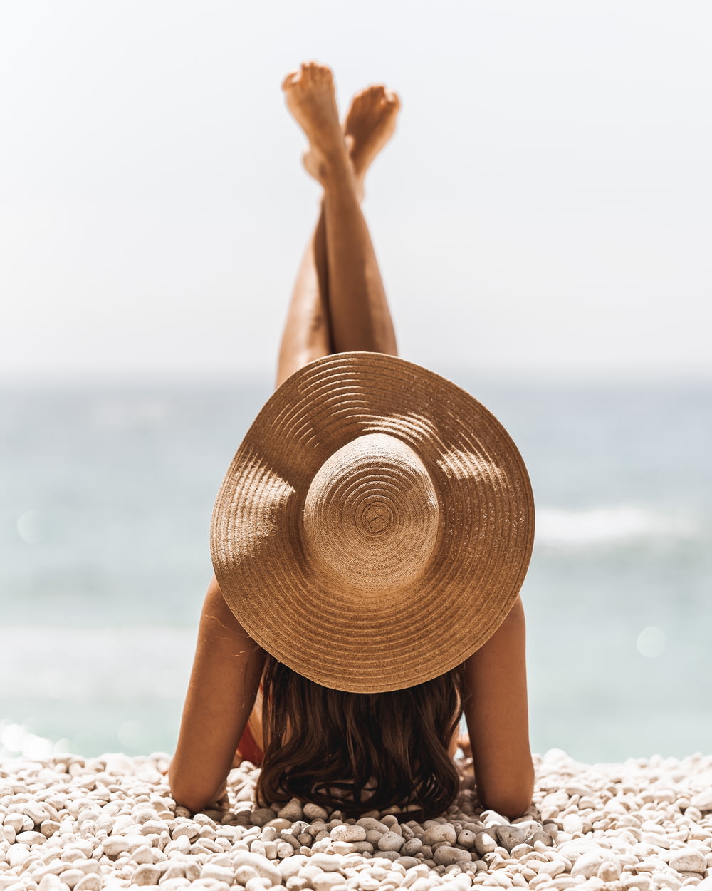 日中のビーチに立つ茶色の日よけ帽をかぶった女性