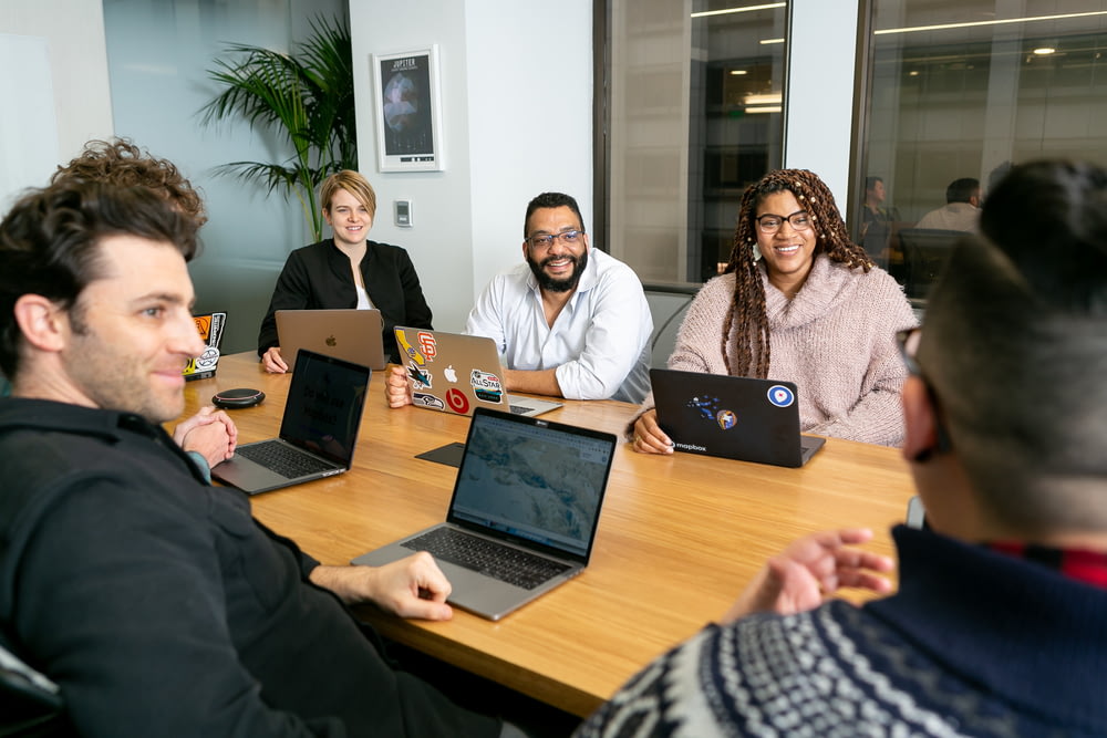 Quatre personnes, toutes sur des ordinateurs portables, deux hommes et deux femmes, écoutent une personne parler lors d’une réunion du conseil d’administration 