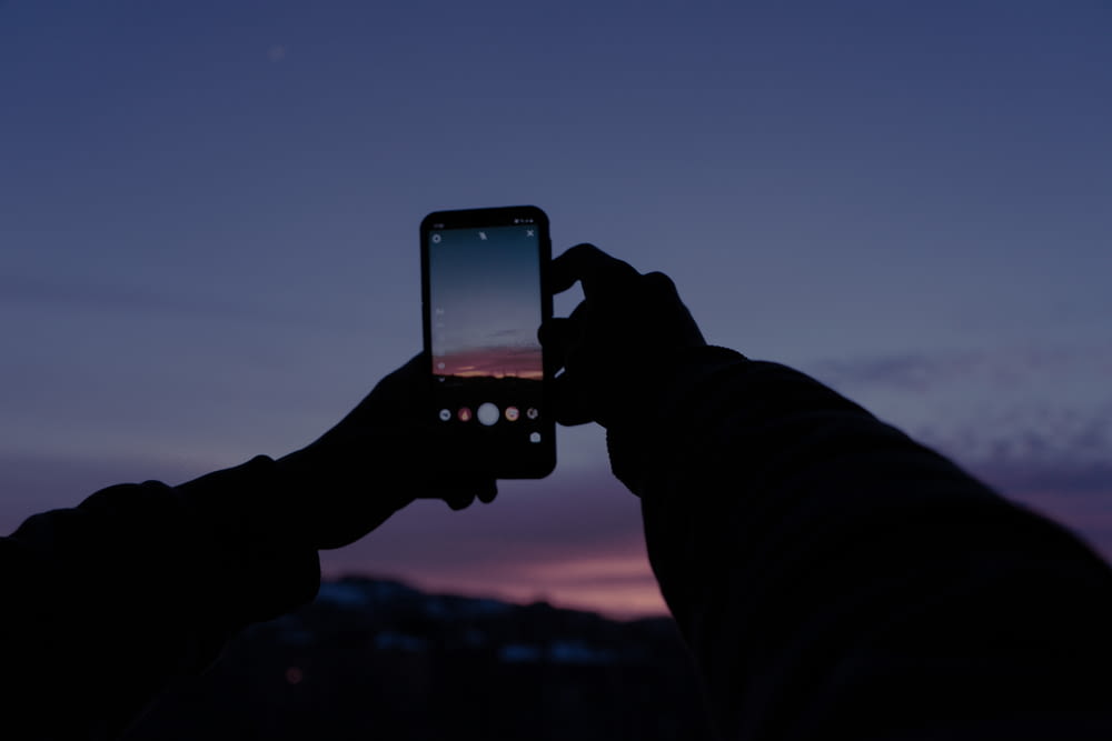 person holding black iphone 4 taking photo of sunset