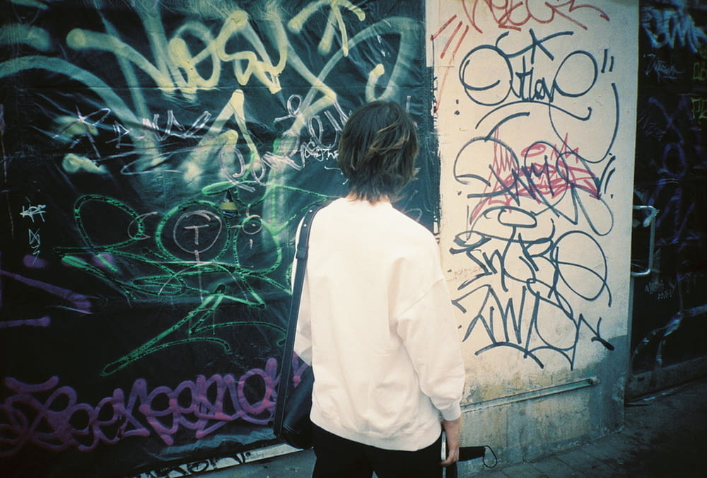 woman in white long sleeve shirt and black pants standing in front of graffiti wall