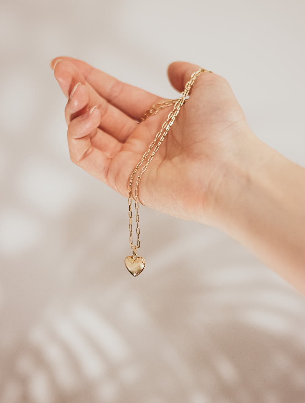 uma mão segurando um amuleto de coração de ouro em uma corrente