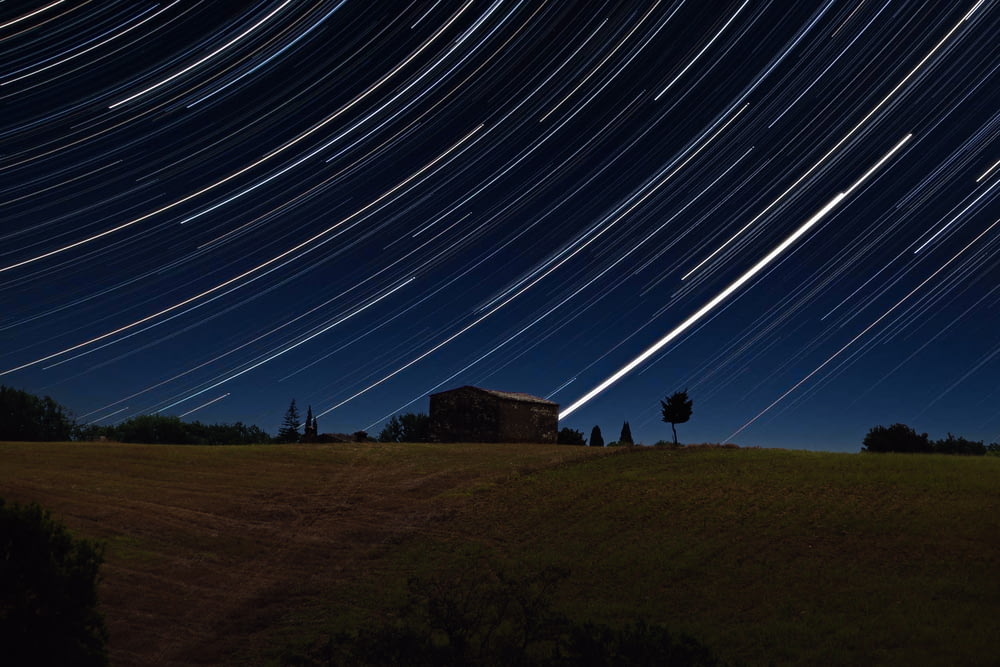 the night sky with a star trail over a field