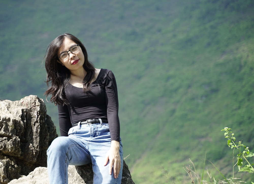 a woman sitting on top of a rock next to a lush green hillside
