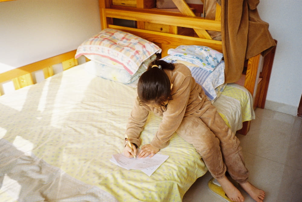 a little girl sitting on a bed writing on a piece of paper