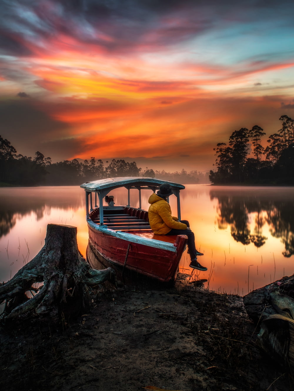 uomo in camicia rossa che si siede sulla barca durante il tramonto