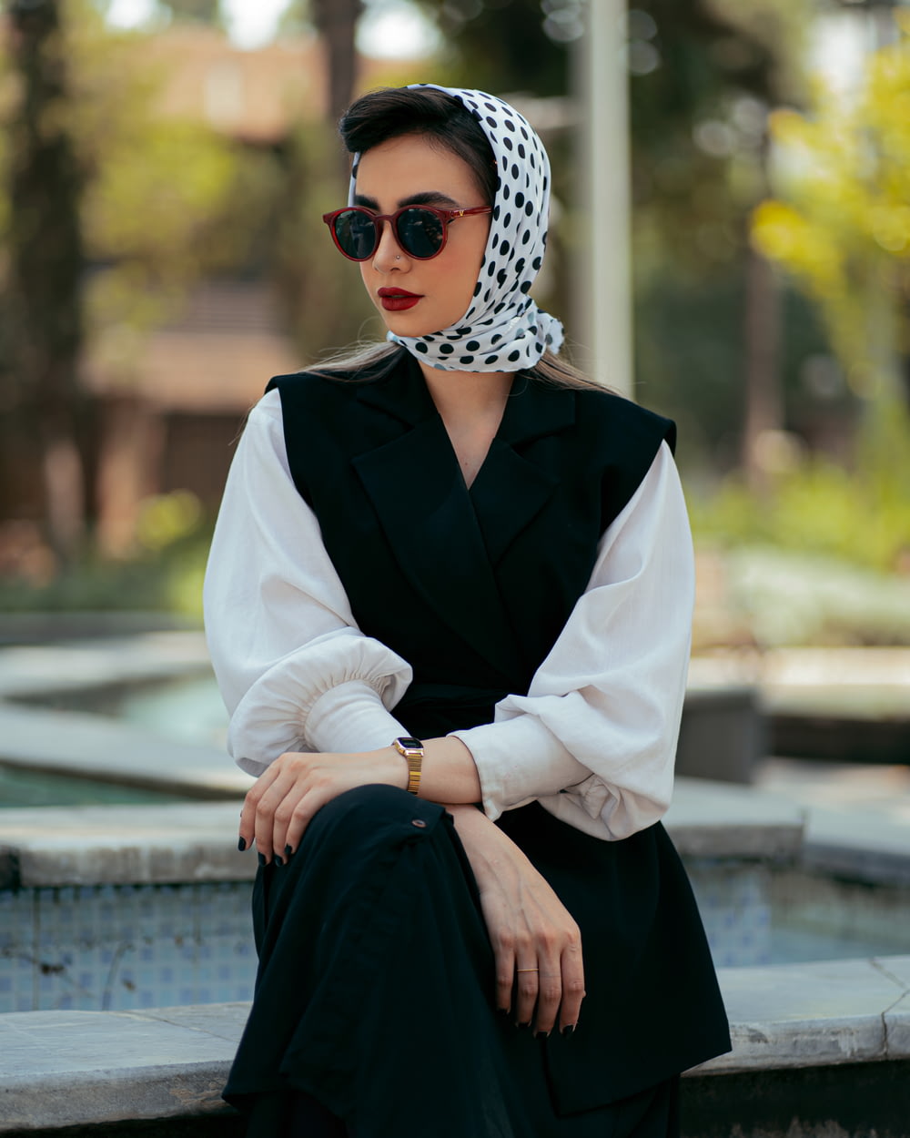 a woman sitting on a ledge wearing sunglasses and a scarf