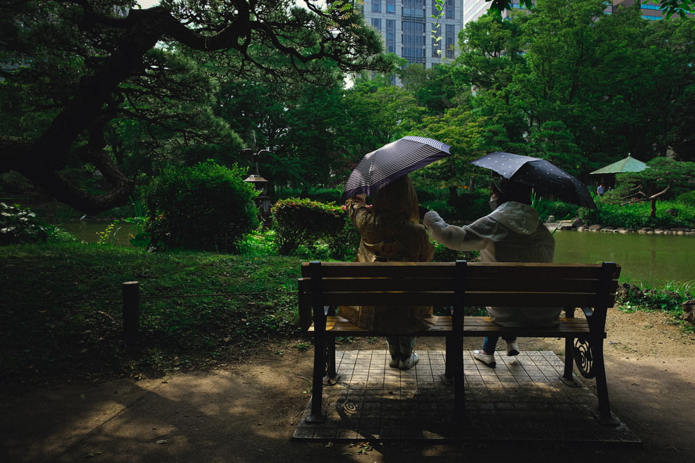 man in brown jacket sitting on brown wooden bench under umbrella during daytime