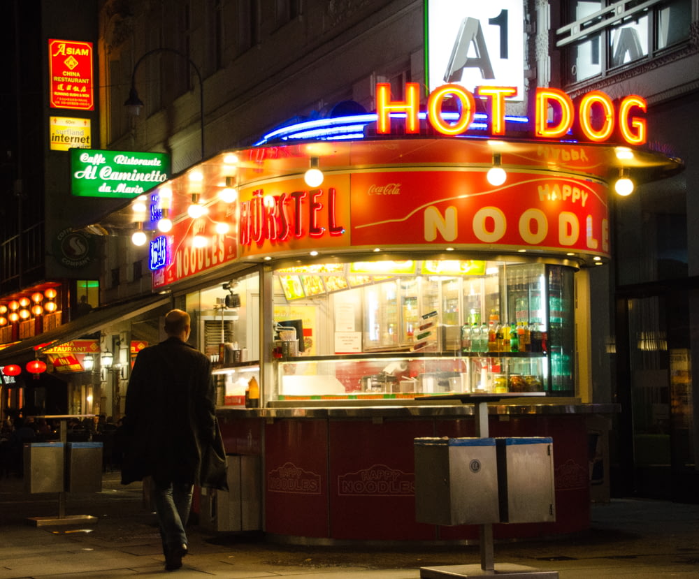 a man walking down the street in front of a hot dog stand