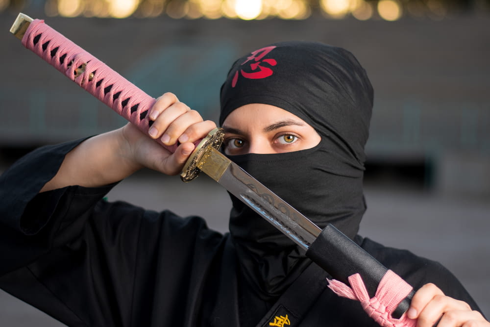 mulher no hijab preto segurando a espada rosa e preta