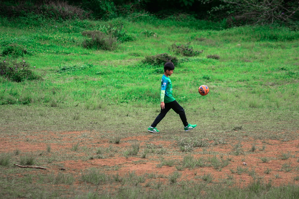 boy in blue shirt and black pants playing soccer during daytime