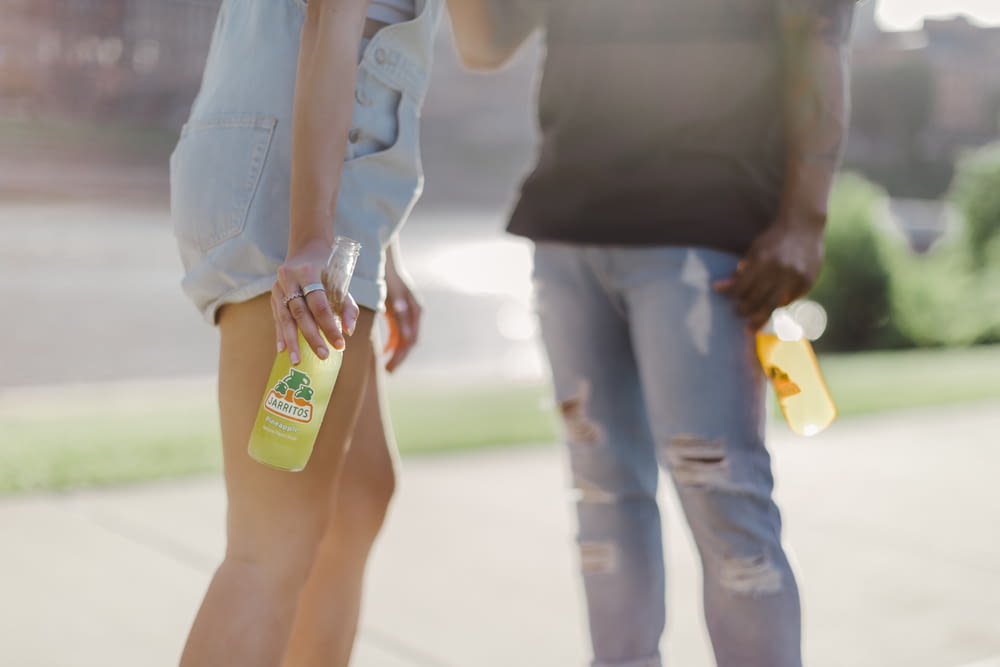 woman in black tank top and blue denim jeans holding yellow and green plastic bottle