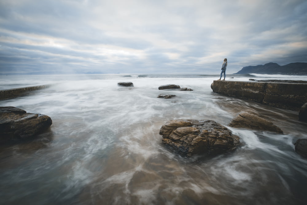 person standing on rock formation in the middle of sea during daytime