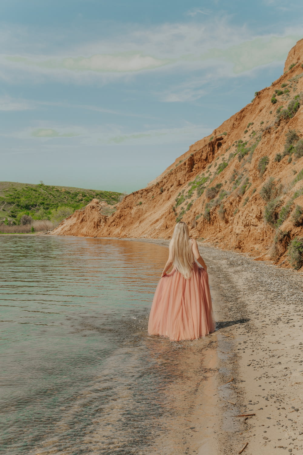woman in pink dress standing on gray sand near body of water during daytime