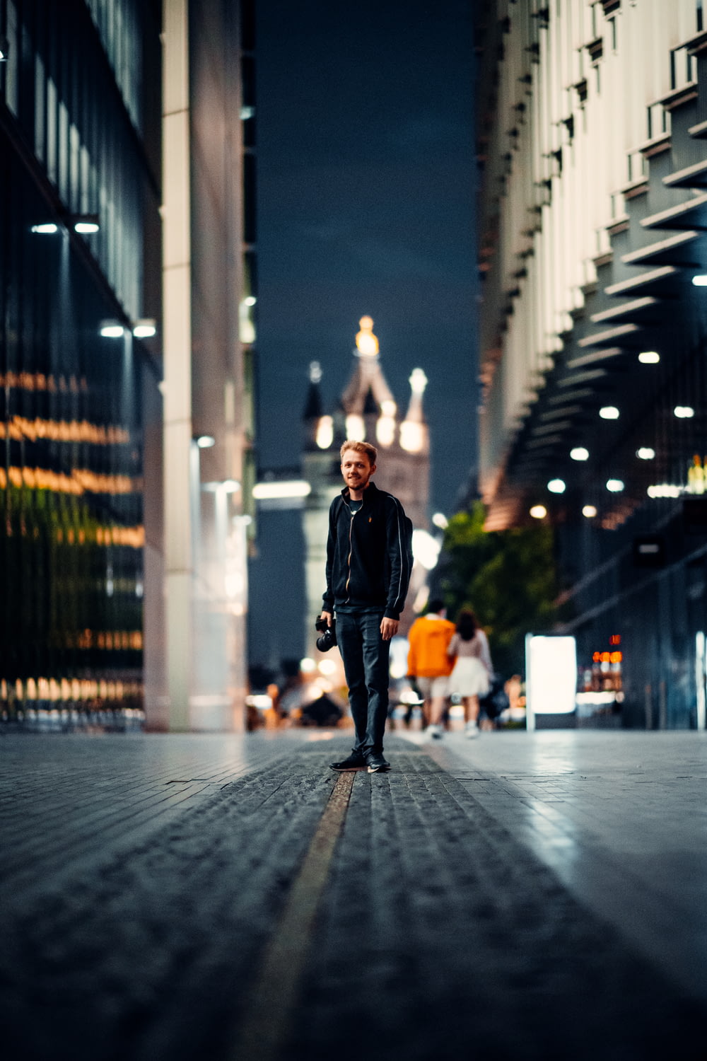 man in black jacket and black pants standing on sidewalk during night time
