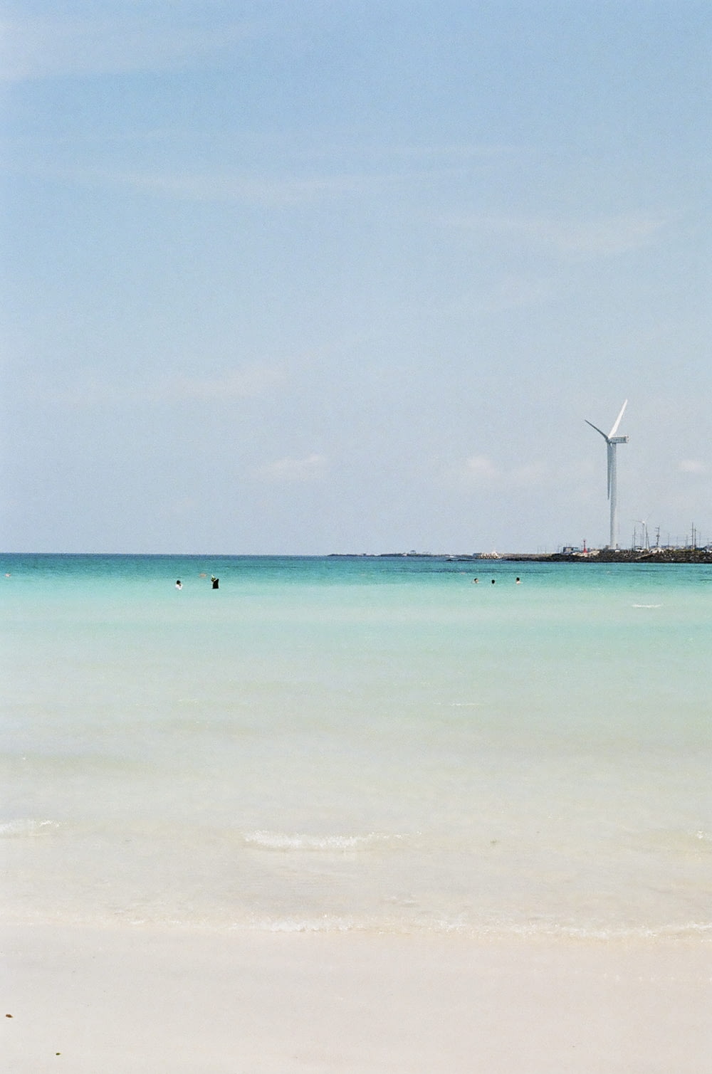 white wind turbines on green sea under blue sky during daytime