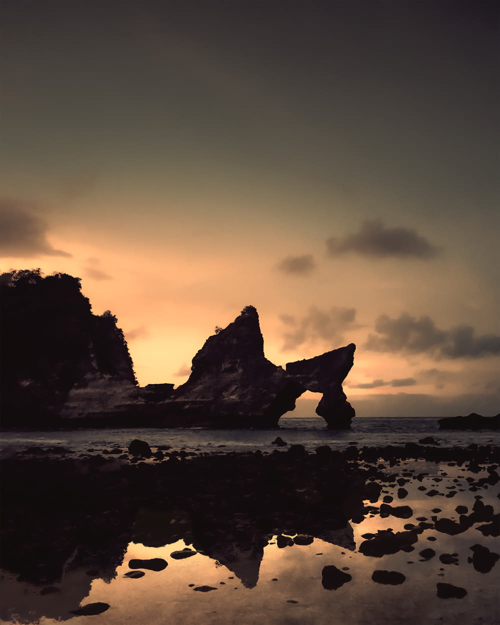 silhouette of rock formation on sea shore during sunset