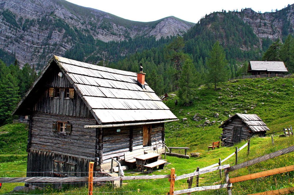 Maison en bois gris sur un champ d’herbe verte près des arbres verts et de la montagne pendant la journée