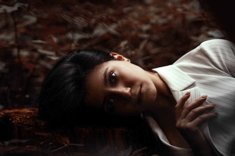 woman in white button up shirt lying on dried leaves
