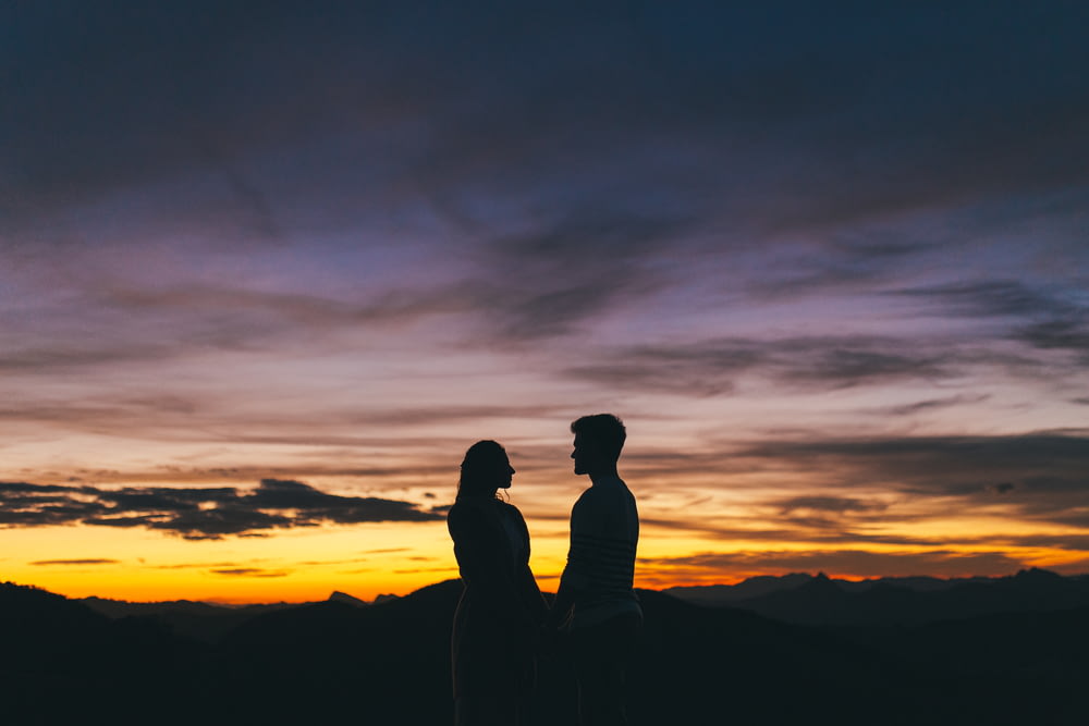 silhouette of couple standing on mountain during sunset