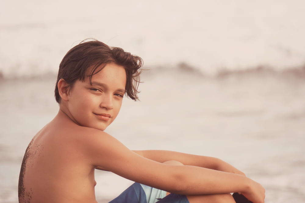 a young boy sitting on a beach next to the ocean