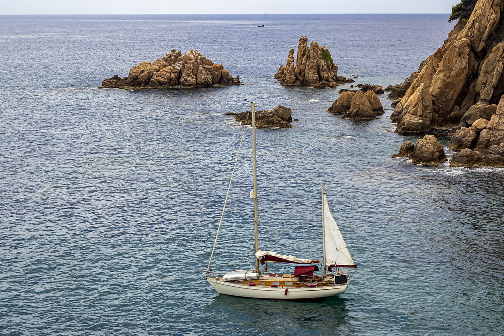 a sailboat in the ocean with rocks in the background