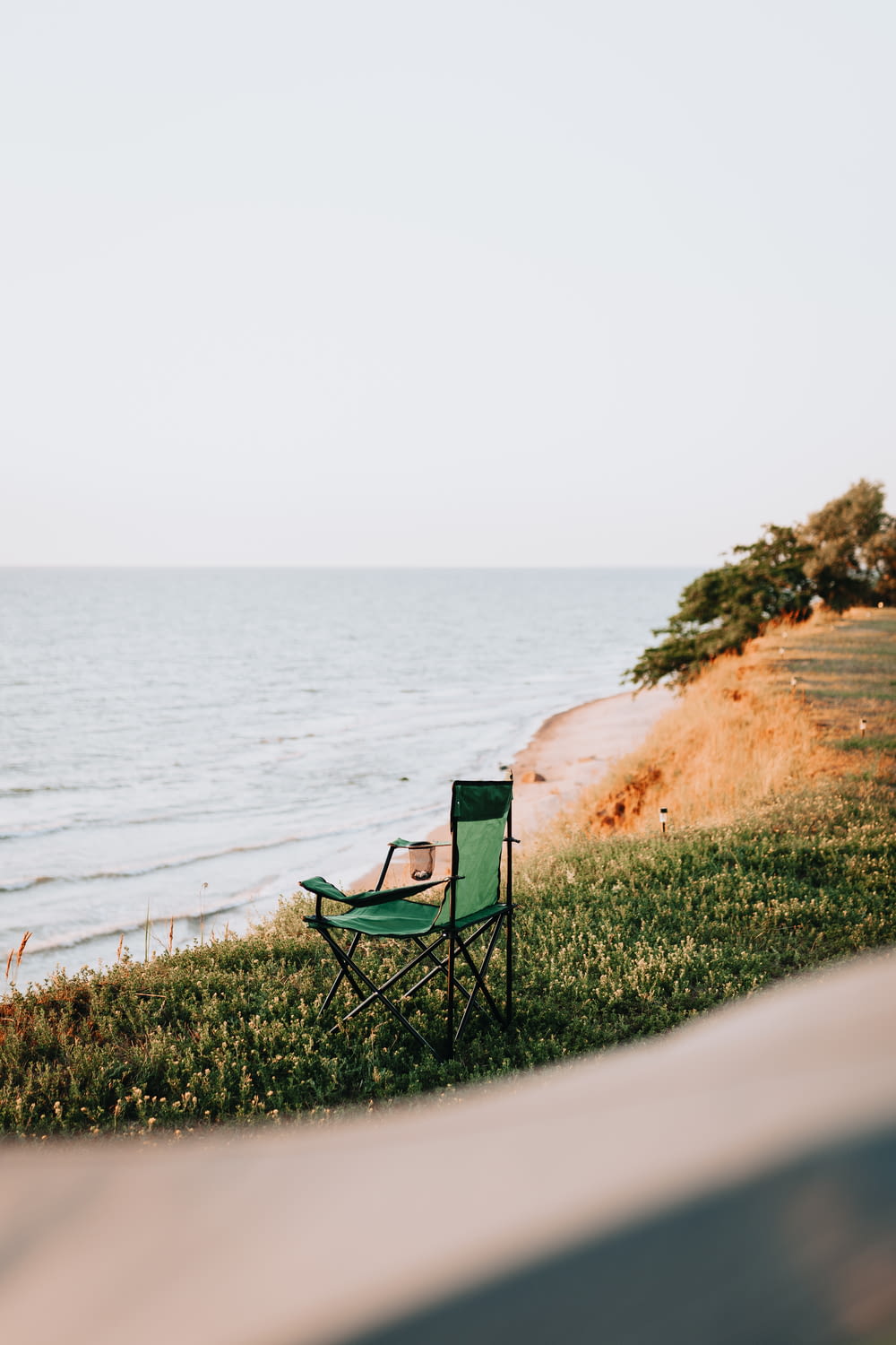 chaise de camping verte et noire sur le sable brun près du plan d’eau pendant la journée