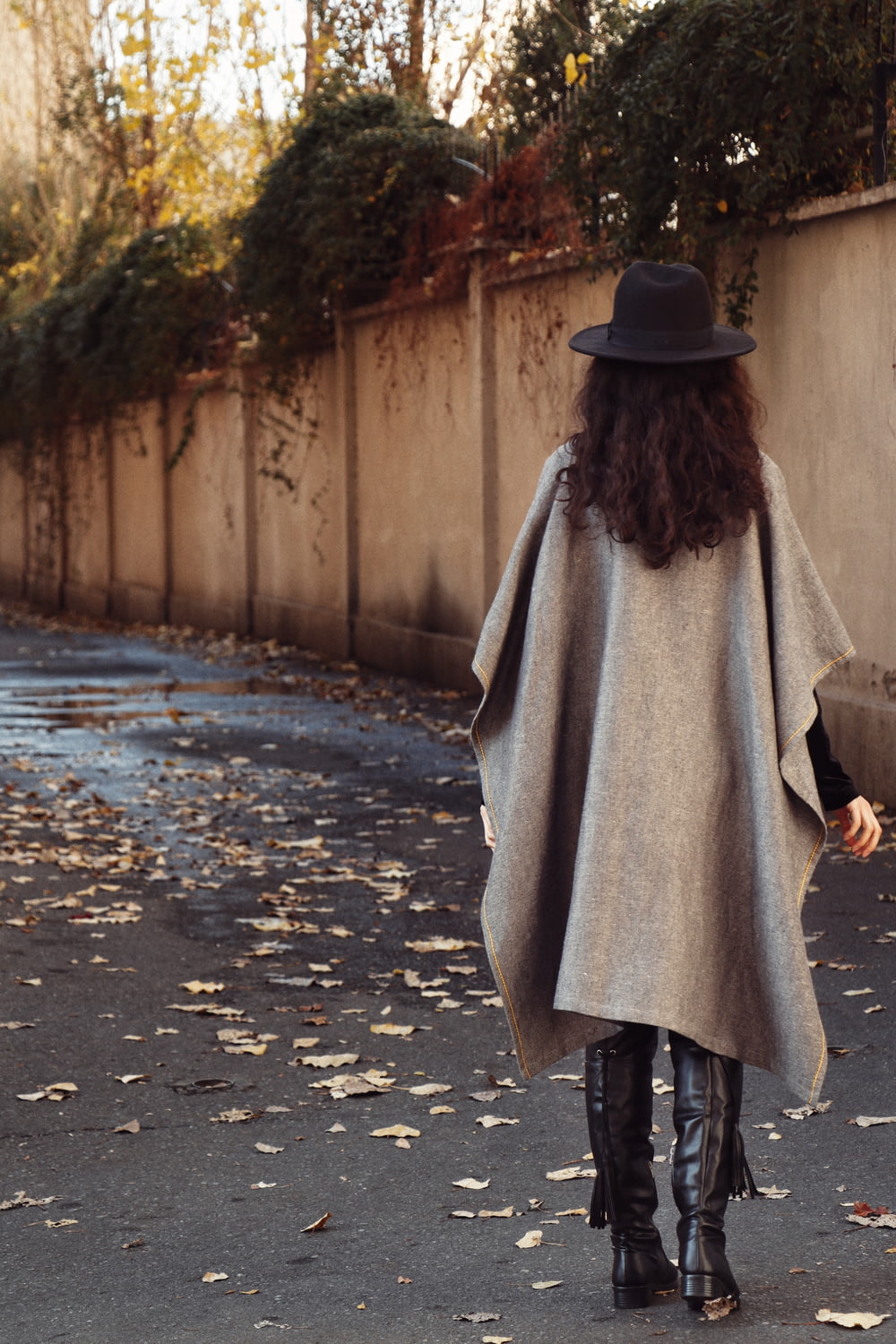 검은 모자와 회색 코트를 입은 여자가 낮 동안 거리를 걷고 있다