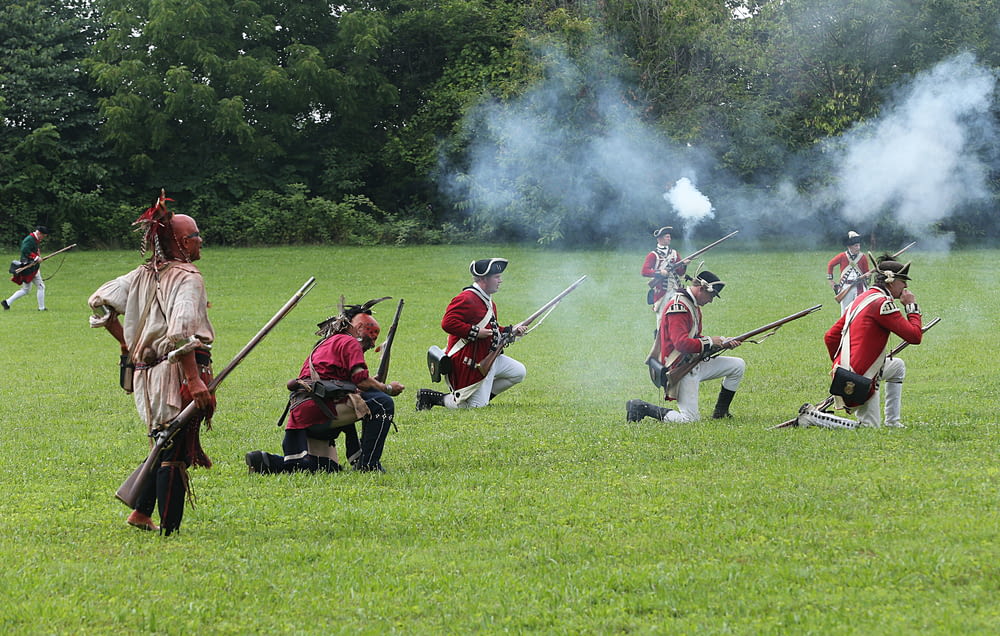 people in red and black robe holding rifle on green grass field during daytime