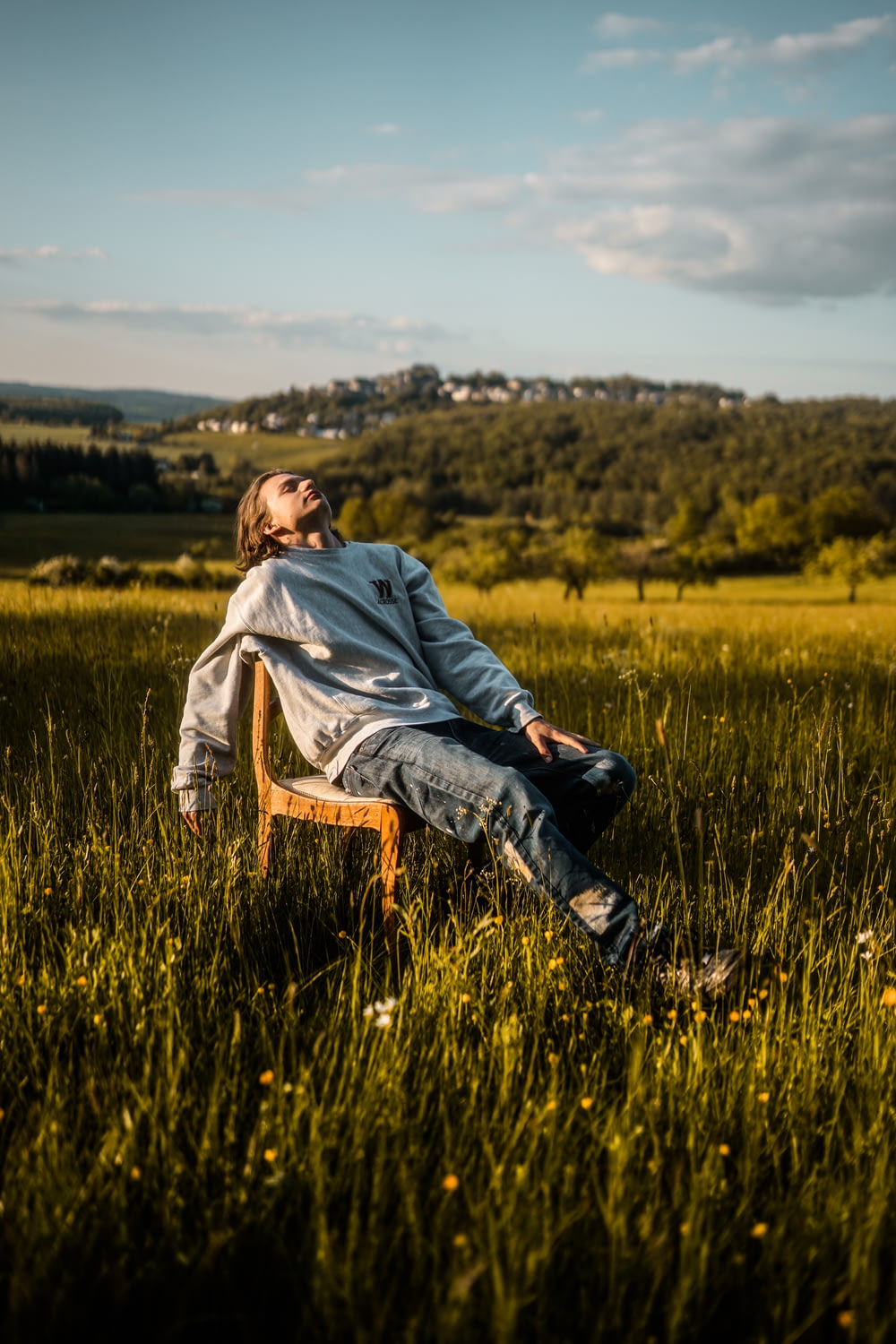 homem em capuz cinza sentado na cadeira de madeira marrom no campo de grama verde durante o dia