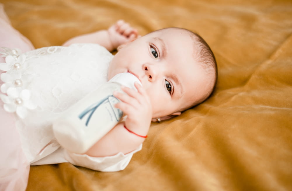 baby in white dress lying on yellow textile