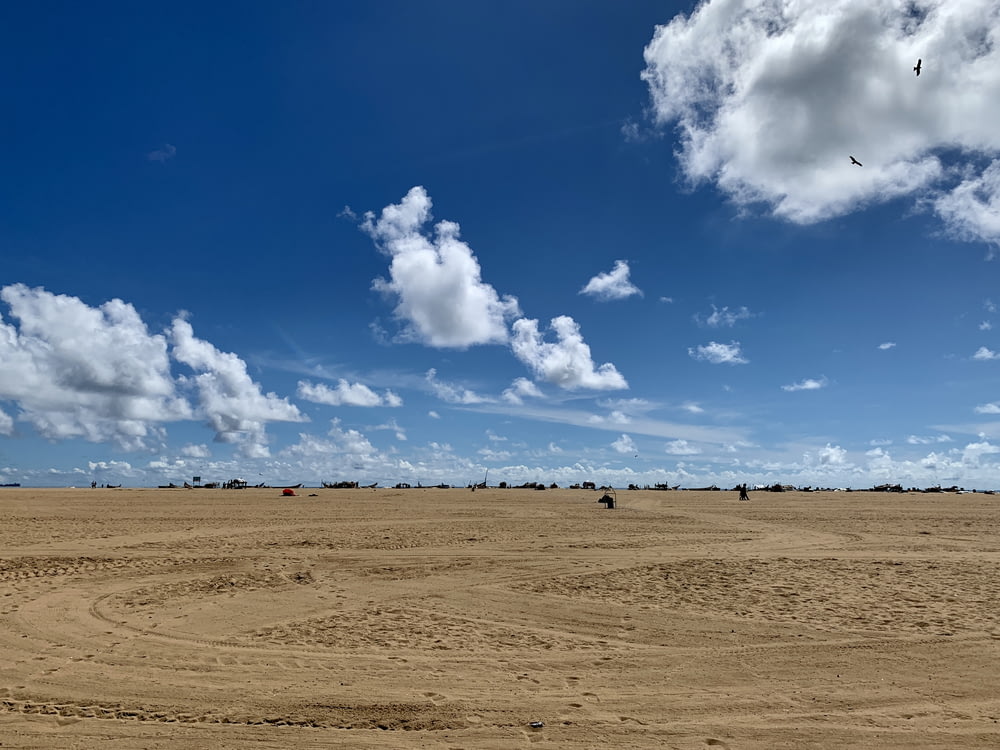 people on brown sand under blue sky and white clouds during daytime