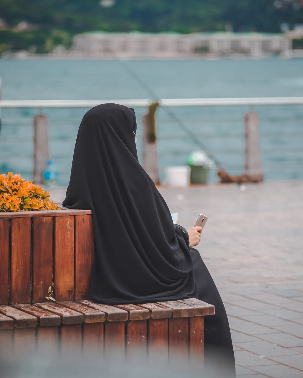 Frau im schwarzen Hijab sitzt auf brauner Holzbank