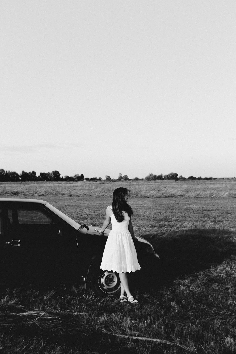 woman in white dress standing beside black car