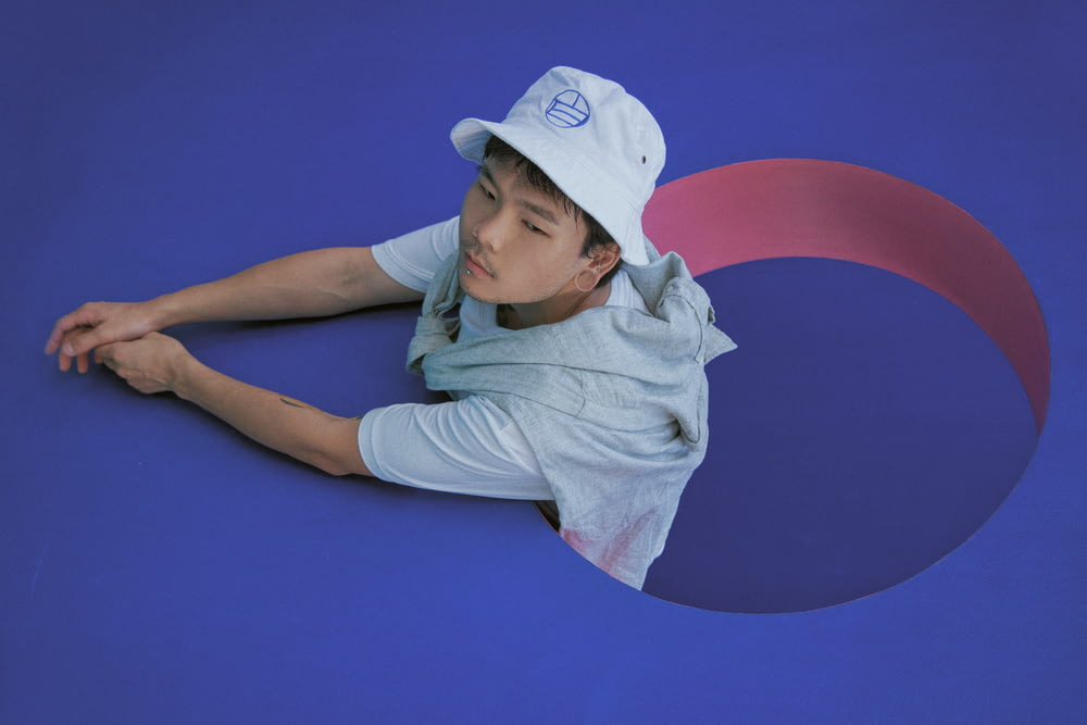woman in white shirt and white cap lying on blue wall