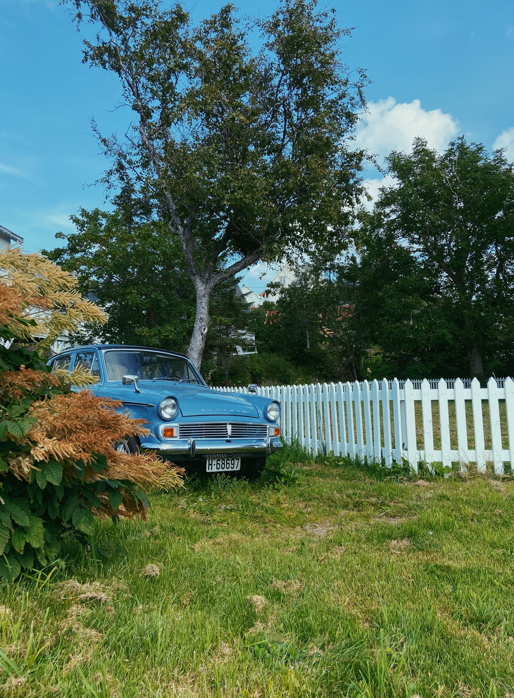 blue car parked beside white wooden fence during daytime