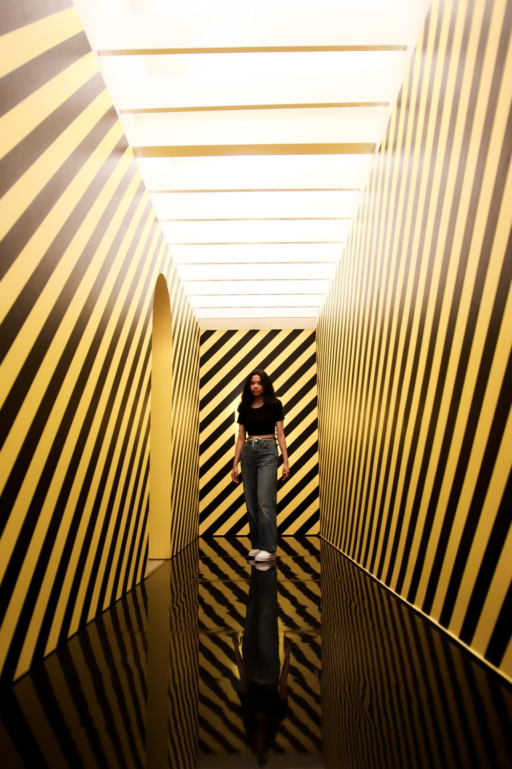 woman in black jacket and blue denim jeans standing on white and brown stripe tunnel