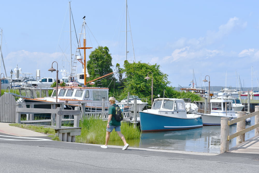 homem de camisa verde andando na rua perto do barco branco e azul durante o dia